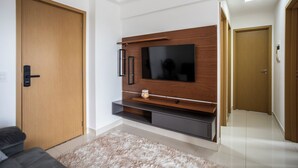Uma sala de estar moderna com uma TV de tela plana fixada em uma parede de madeira, um sofá escuro e um tapete fofo.