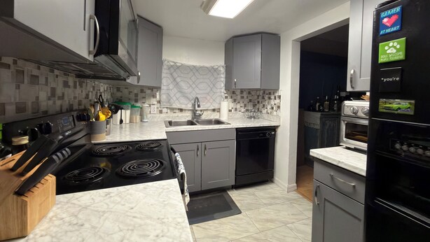 A modern kitchen with grey cabinets, a black refrigerator, and a built-in oven. - Affordable private room King bed in Thonotosassa, shared space (Thonotosassa)