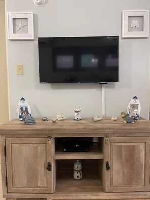 Een televisie bevestigd aan een wand boven een houten kastje met decoratieve objecten erop.