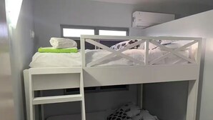 Camera con letto a castello, una finestra, uno scaffale bianco e un oggetto blu sul letto inferiore.