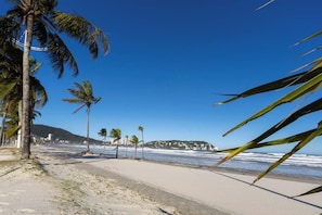 A beach with palm trees, a clear blue sky, and a distant mountain. - Amazing Spacious House 200m from Enseada Beach (Guarujá)