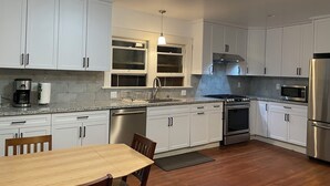 A modern kitchen with white cabinets, a stainless steel refrigerator, a microwave, a stove, and a dining table with chairs. - Charming 3-bedroom apartment near Piedmnot and Oakland with AC for your stay (Oakland)