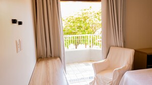 A room with a balcony, a white chair, a bed, and a wooden nightstand. - Casa c/ Piscina a 550m da Praia | Até 10 hóspedes (Lauro de Freitas)