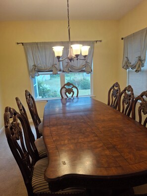 Un comedor con una gran mesa de madera, sillas ornamentadas, una araña y una ventana con cortinas.