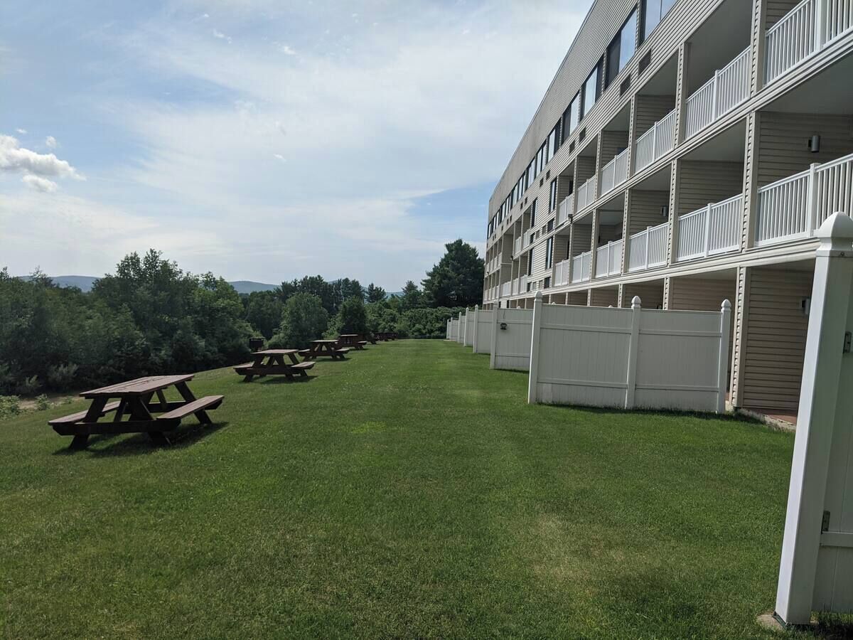 A building with multiple balconies and a grassy area with picnic tables.