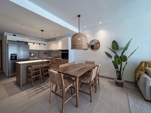 Eine moderne Küche mit Kochinsel, Essbereich mit Holztisch und einer großen Topfpflanze.