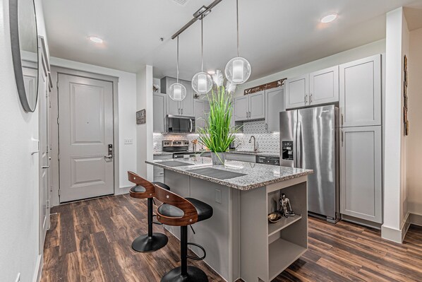 A modern kitchen with a central island, bar stools, stainless steel appliances, and a decorative plant. - Peaceful cozy retreat (Addison)