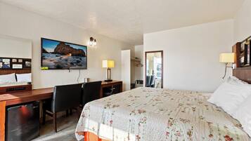 A hotel room with a bed, desk, chairs, and a television.