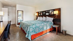 A hotel room with a bed, a wooden nightstand, a table, and a trash can. - Temple View Inn Ogden (Ogden)