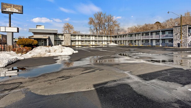 A motel with a two-story structure, a parking lot with puddles, and a signboard. - Temple View Inn Ogden (Ogden)