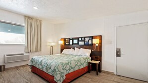 A hotel room with a bed, bedside tables, a wall-mounted artwork, a window with curtains, and a door. - Temple View Inn Ogden (Ogden)