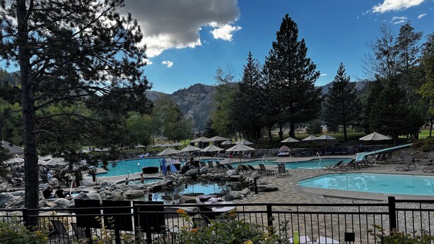 A pool area with multiple pools, lounge chairs, umbrellas, and a mountainous backdrop.