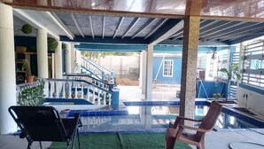 A covered outdoor area with a pool, two chairs, and a staircase leading to a building. - Hotel Rio Maria (La Ceiba)