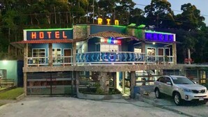 A hotel with a sign reading "HOTEL" and "MARINA" in neon lights, featuring a balcony and a car parked in front. - Hotel Rio Maria (La Ceiba)