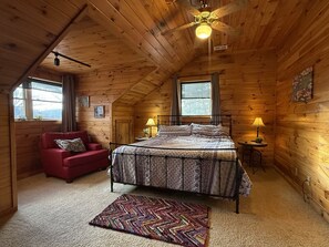 Une chambre confortable dans un chalet en bois, avec un lit, un canapé rouge, une petite table et un ventilateur de plafond.