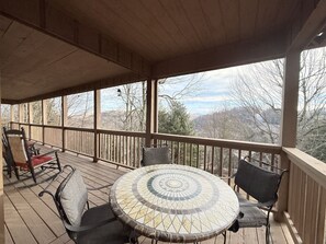 Un espace extérieur abrité, doté d’une table ronde et de chaises, d’une terrasse en bois et offrant une vue sur les arbres et les collines.