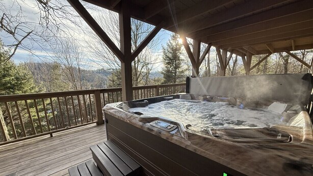 Een hottub met een houten terras en uitzicht op bomen en bergen.