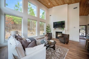 A spacious living room with a fireplace, large windows, and a television. - Hot Tub,  Barrel Sauna, Couples Retreat Broken Bow (Broken Bow)