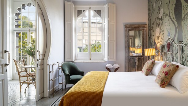 Ein Schlafzimmer mit Bett, Stuhl, Fenster und Blick ins Freie.