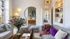 Ein Wohnzimmer mit einer Couch, Poufs, einem Couchtisch mit Blumenvase, einem Kamin und einem Bücherregal.