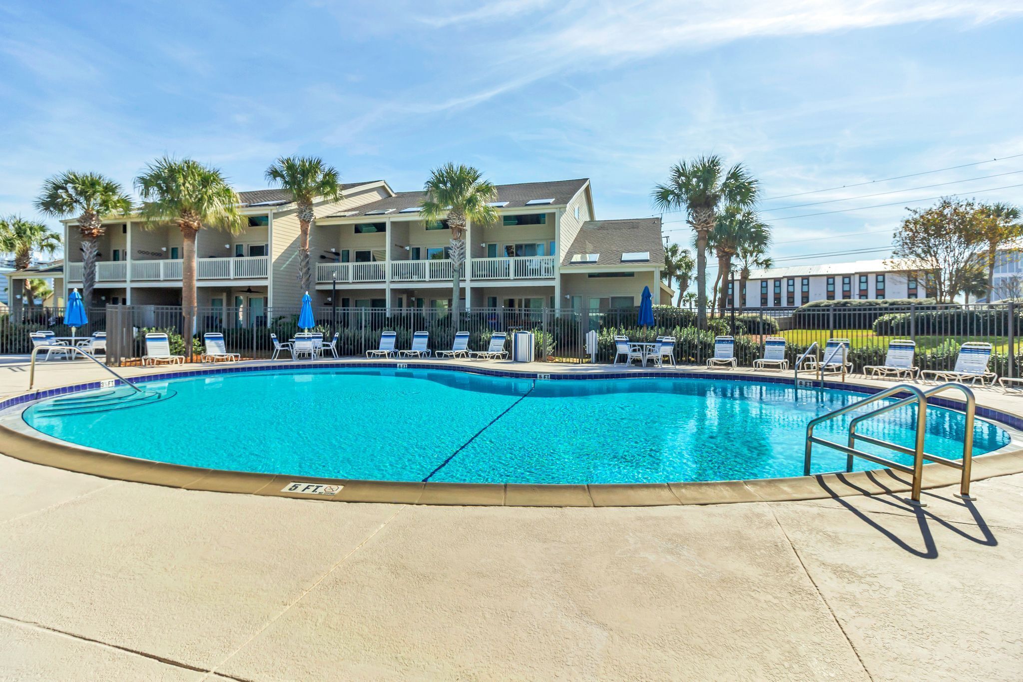 A swimming pool with lounge chairs and palm trees, surrounded by a building with balconies.