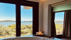 A room with a large bathtub, a view of a lake, and a door leading outside. - HOSPEDARIA PONTA DA PITEIRA (Imbituba)