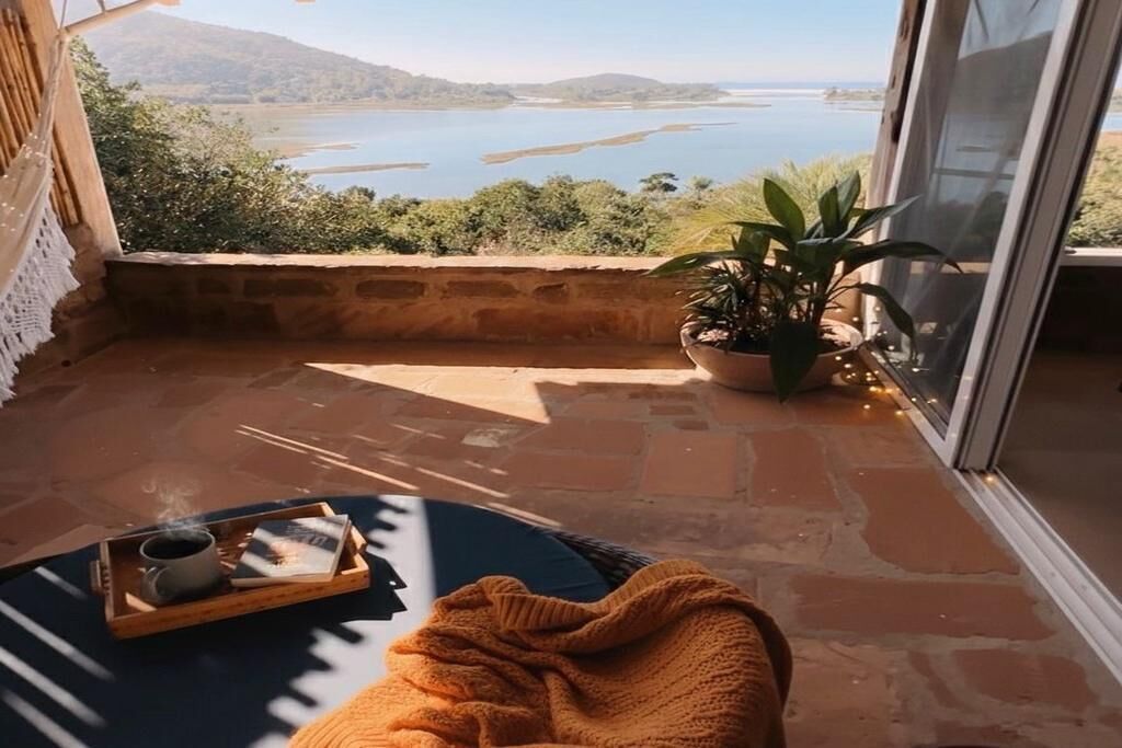 Un balcón con vistas a un lago, una planta en maceta y una bandeja con una taza y un libro.