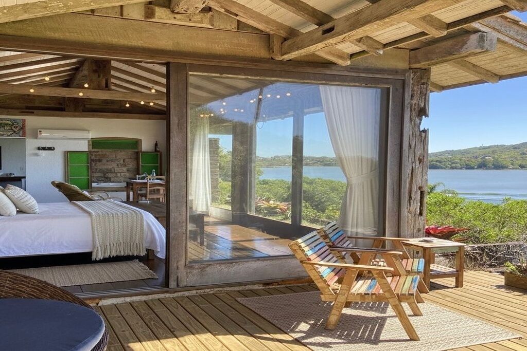 Quarto com cama, escrivaninha e vista para um lago.
