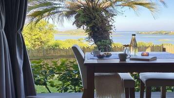 Una mesa de comedor con sillas, una vela y vistas a un paisaje tropical con una palmera y agua.