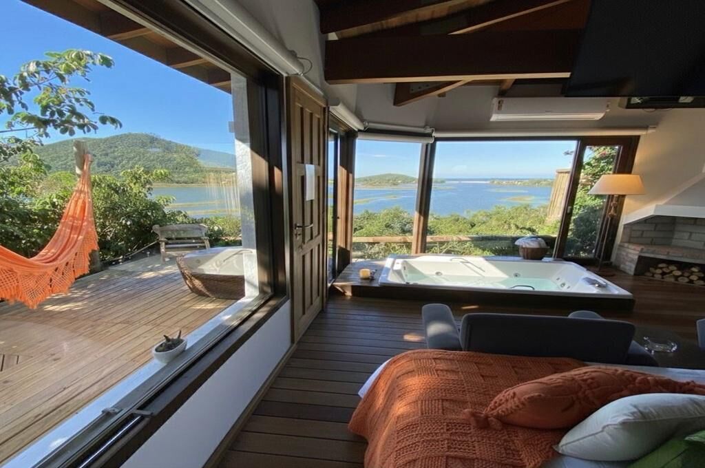 Un dormitorio con un ventanal grande, una hamaca, un jacuzzi y vistas a un lago.