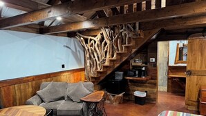 Una habitación acogedora con una escalera de madera, un sofá, una mesa de centro y una alfombra a rayas.