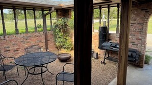 Un patio exterior con una mesa redonda y sillas, un muro de ladrillo y una zona de barbacoa.