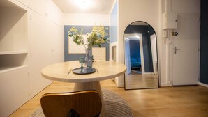 A dining area with a round table, a vase with flowers, and a mirror on the wall. - L'Ecrin Bleu - Spacious - Ideal for couples & professionals - WiFi - Station & Hyper center (Angoulême)