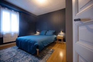 Ein Schlafzimmer mit einem Bett, Nachttischlampen, einem Nachttisch, einem Heizkörper und einem Fenster mit Vorhängen.