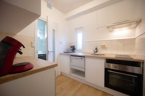 A compact kitchen with white cabinets, a dishwasher, an oven, and a red coffee maker on the counter. - L'Ecrin Bleu - Spacious - Ideal for couples & professionals - WiFi - Station & Hyper center (Angoulême)