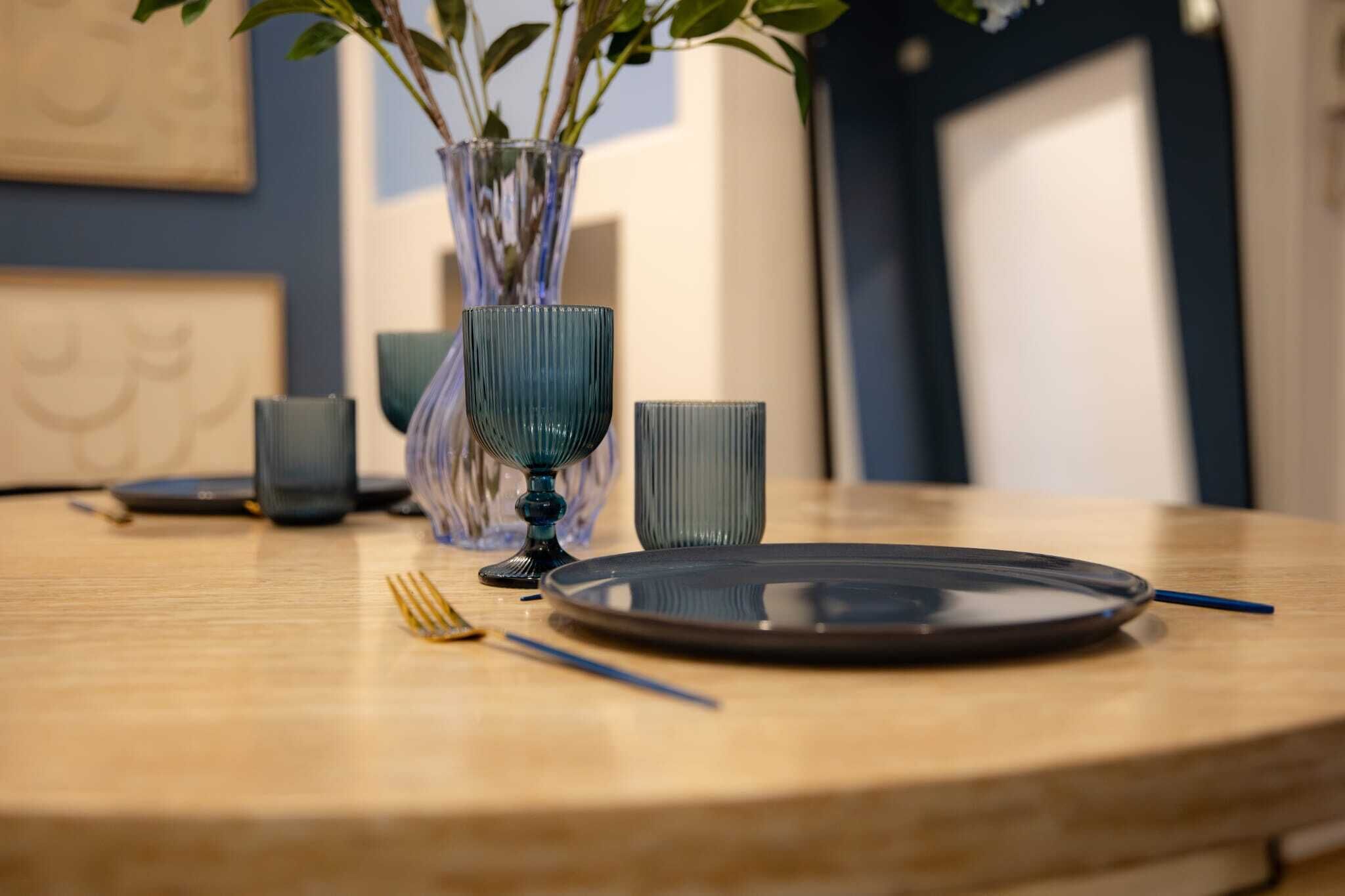 A dining table with a plate, a fork, a knife, and a vase with plants.
