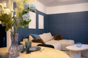 A living room with a beige sofa, a round table with a vase and plates, and a blue accent wall. - L'Ecrin Bleu - Spacious - Ideal for couples & professionals - WiFi - Station & Hyper center (Angoulême)