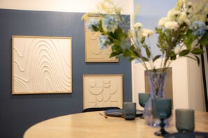 A dining area with a round table, three framed wall art pieces, and a vase with flowers. - L'Ecrin Bleu - Spacious - Ideal for couples & professionals - WiFi - Station & Hyper center (Angoulême)