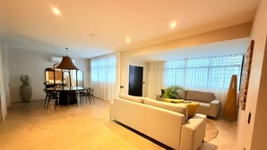 En moderne stue med sofa, spisebord og stole. Der er et stort vindue med gardiner og en plante på sofaen.