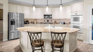 A modern kitchen with white cabinetry, stainless steel appliances, a granite countertop island, and pendant lighting. - Pool & Spa • Outdoor Fireplace • BBQ • Pool Table (Goodyear)