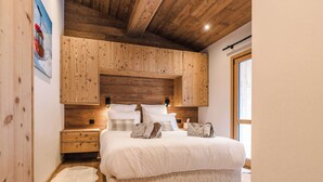 A bedroom with a wooden headboard, a large bed with white bedding, a nightstand, and a window with daylight. - Luxury Chalet with Private Spa & Wellness Area (Megève)