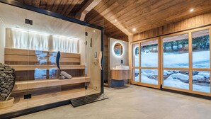A modern spa room with a sauna, a wooden bench, and a view of a snowy landscape through large windows. - Luxury Chalet with Private Spa & Wellness Area (Megève)
