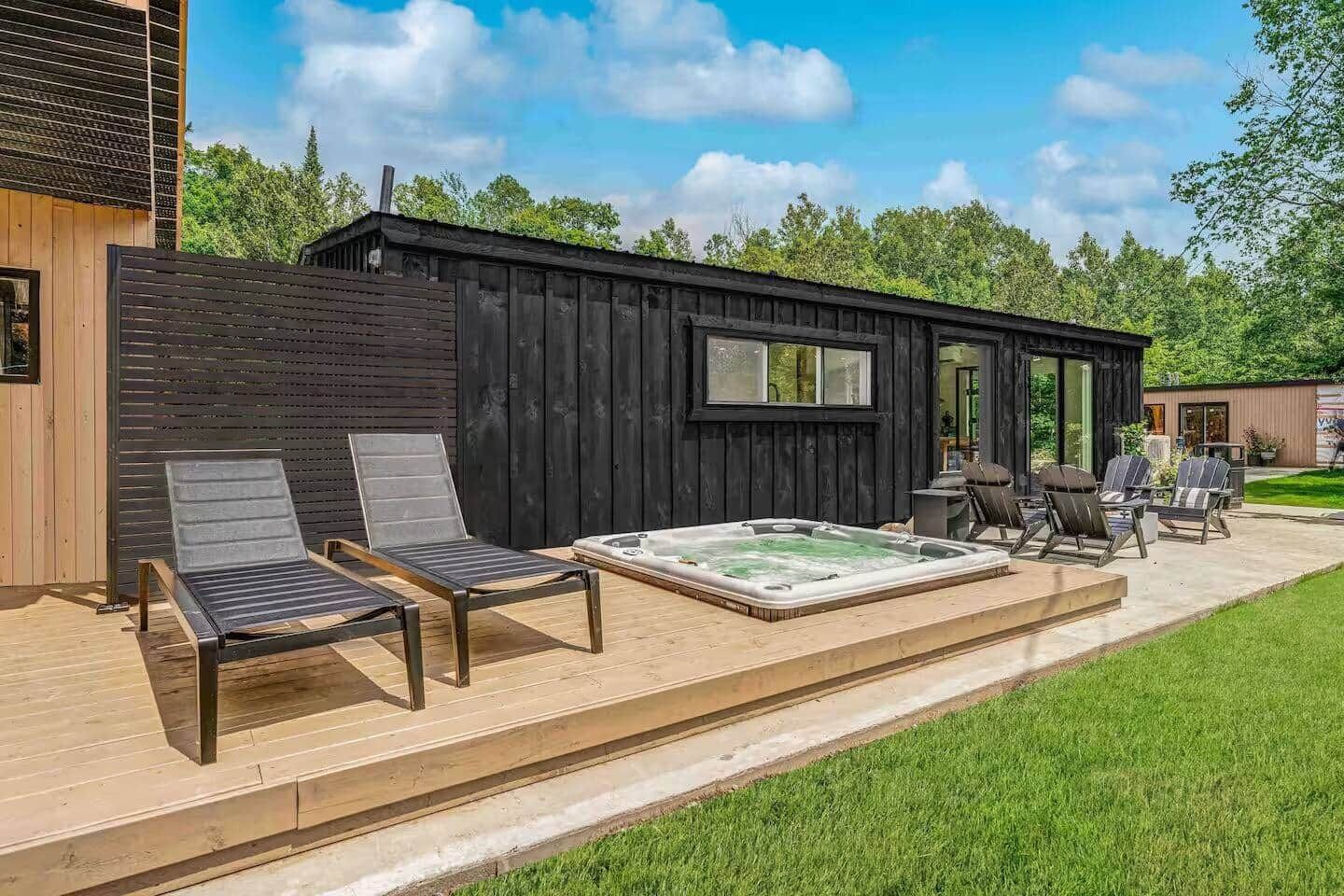 Una baita in legno con idromassaggio, due poltrone relax e un patio.