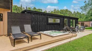 Una baita in legno con idromassaggio, due poltrone relax e un patio.