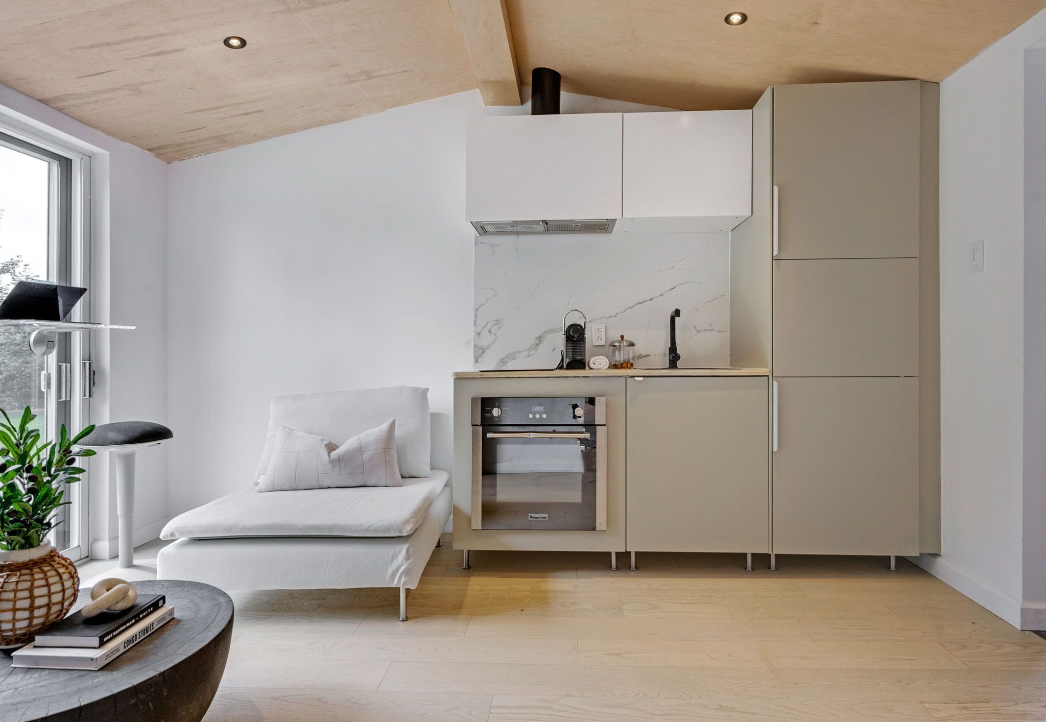 A modern kitchen with built-in appliances, a white sofa, and a dining table with a plant.