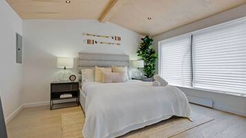 Ein Schlafzimmer mit einem Bett, Nachttischen, einer Lampe, einer Zimmerpflanze und einem Fenster mit Jalousien.