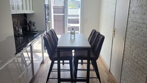 A modern kitchen with white cabinets, a dining table with four chairs, and a brick wall. - House 8 pers - Jacuzzi - Near Lille & Belgium (Tourcoing)