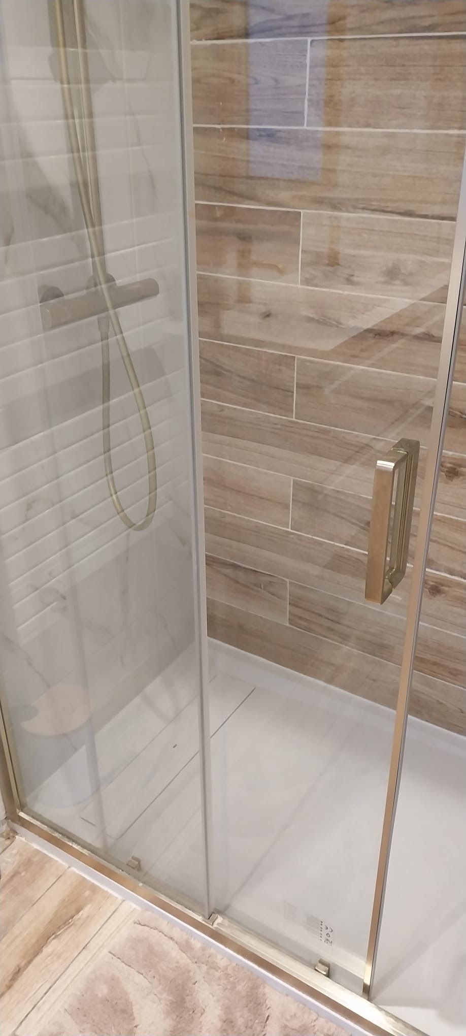 Une douche fermée par des parois de verre, avec un sol en bois et une pomme de douche visible.
