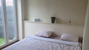 A bedroom with a bed, a window, a door, and a shelf with a picture frame and a cup. - House 8 pers - Jacuzzi - Near Lille & Belgium (Tourcoing)