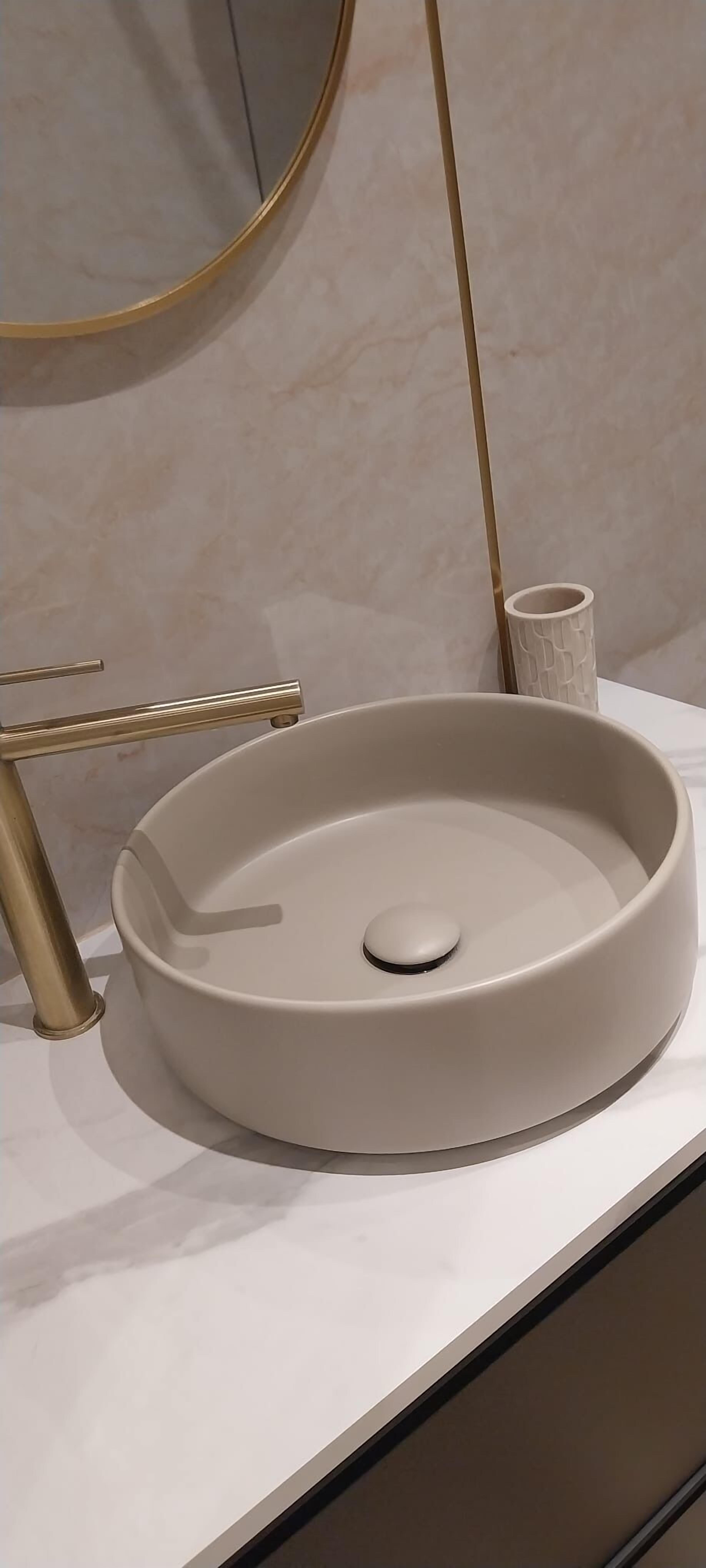 A modern bathroom with a round sink, a gold-colored faucet, and a cylindrical container.